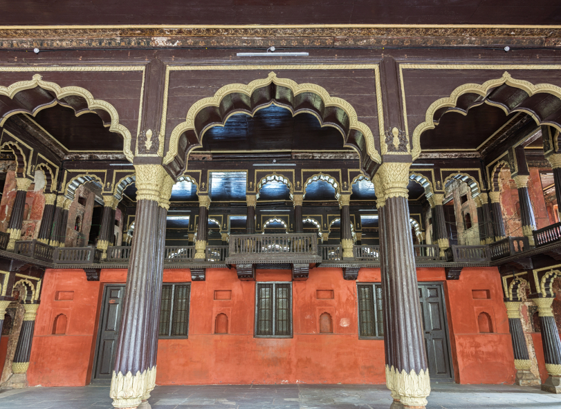 Reception hall and Royal Box at Tipu Sultan Palace in Bengaluru. Teak pillars, red painted walls and cream colored peacock arches.